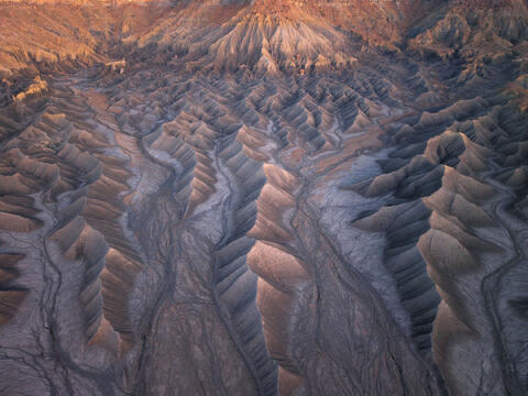A sunrise scene with warm, soft light revealing the layered ridges, eroded slopes, and detailed desert textures of the badlands.