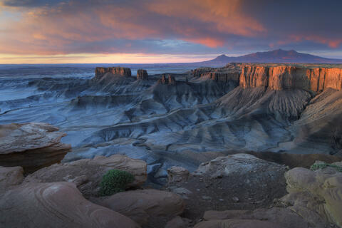 Sunset over the famous Moonscape landscape in Utah, with warm golden light illuminating rugged badlands, layered desert ridges, and dramatic eroded formations.